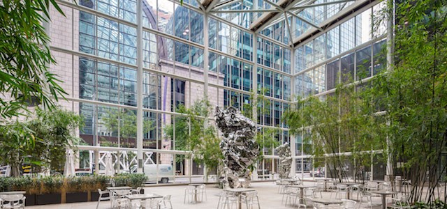 An interior view of the indoor atrium at 590 Madison Avenue with large windows, green trees, and seating areas.