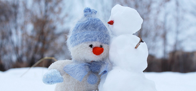 A stuffed snowman wearing a light blue hat leaning up against a real snowman.