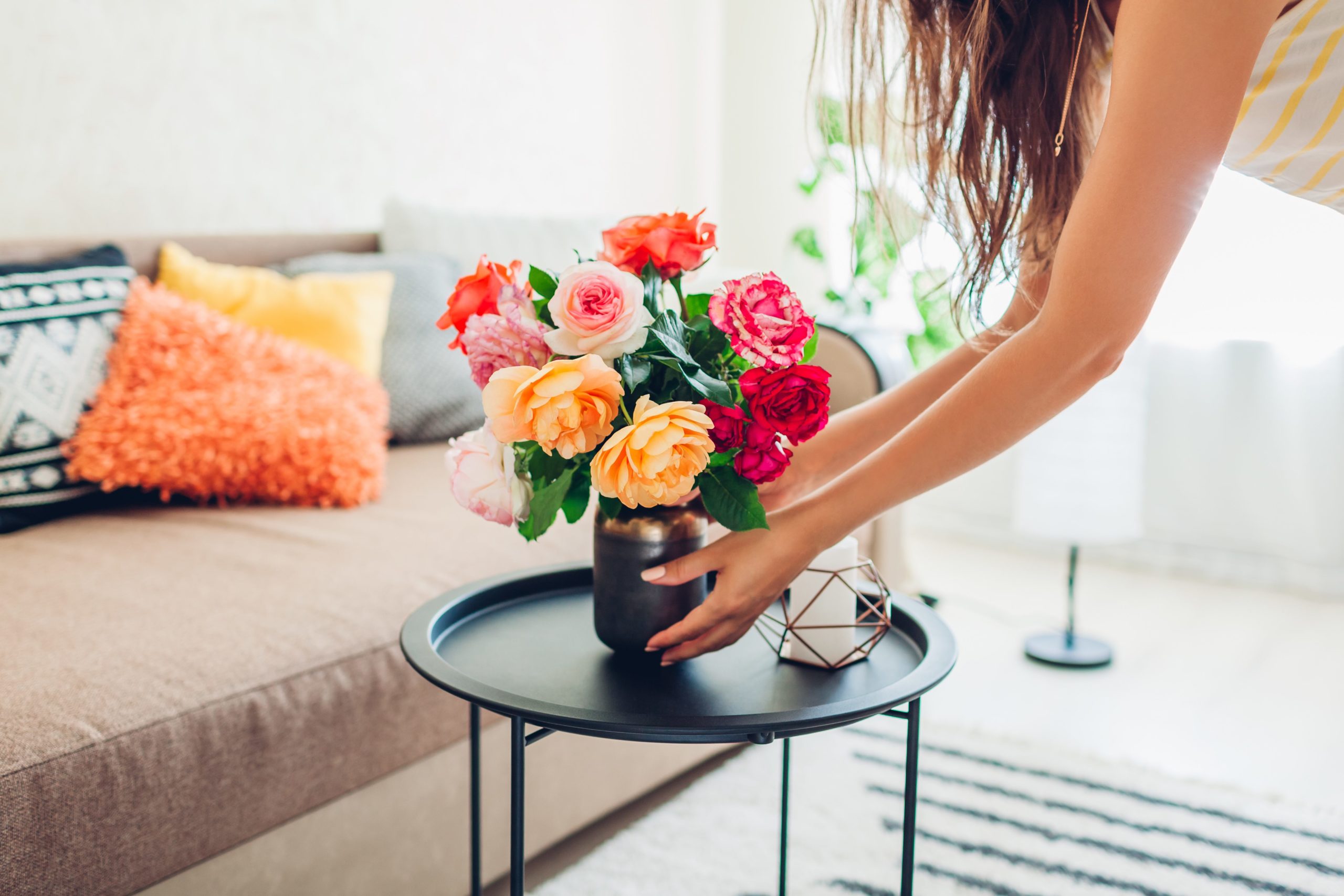 Woman puts vase of red and yellow flowers on her coffee table in living room