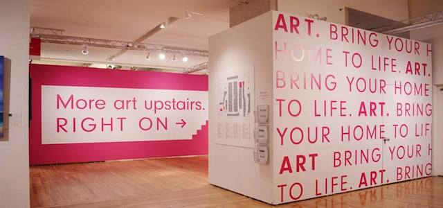 An interior view of The Affordable Art Fair in NYC with hot pink and white wall lettering.