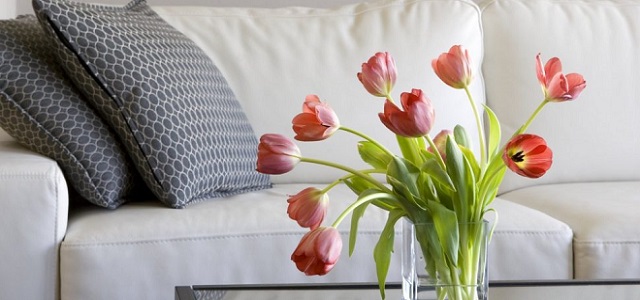 A vase of pink tulips on a glass table with white couch in the background.