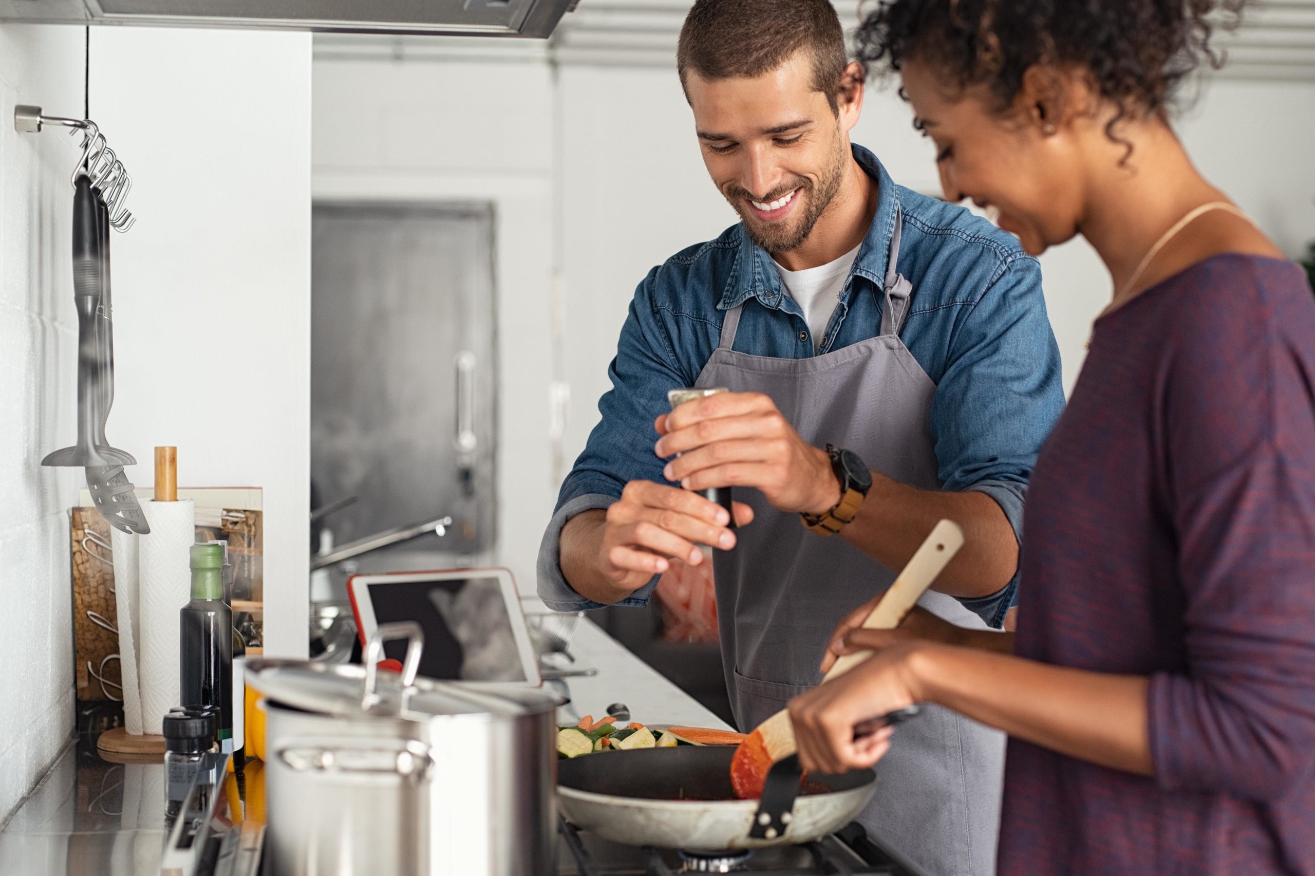 A couple cooking together stirring ingredients into a sauce pan