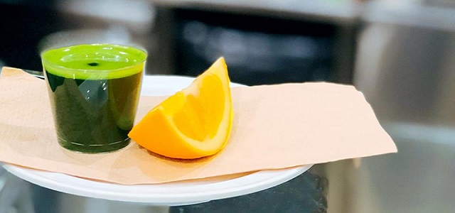 A shot of healthy green juice and an orange slice.