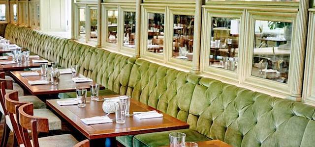 An interior view of Tavern on the Green restaurant n NYC with green booths and warm decor.