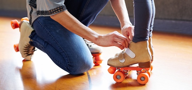 A mother helping her child put on roller skates.