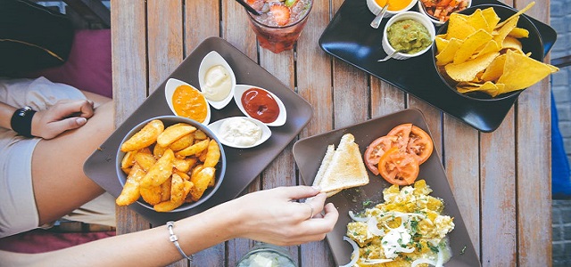 Plates of fresh food on a wooden table with people dipping into.