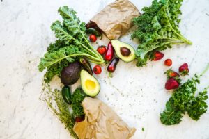 Kale, avocado, peppers and tomatoes on a table with brown bags