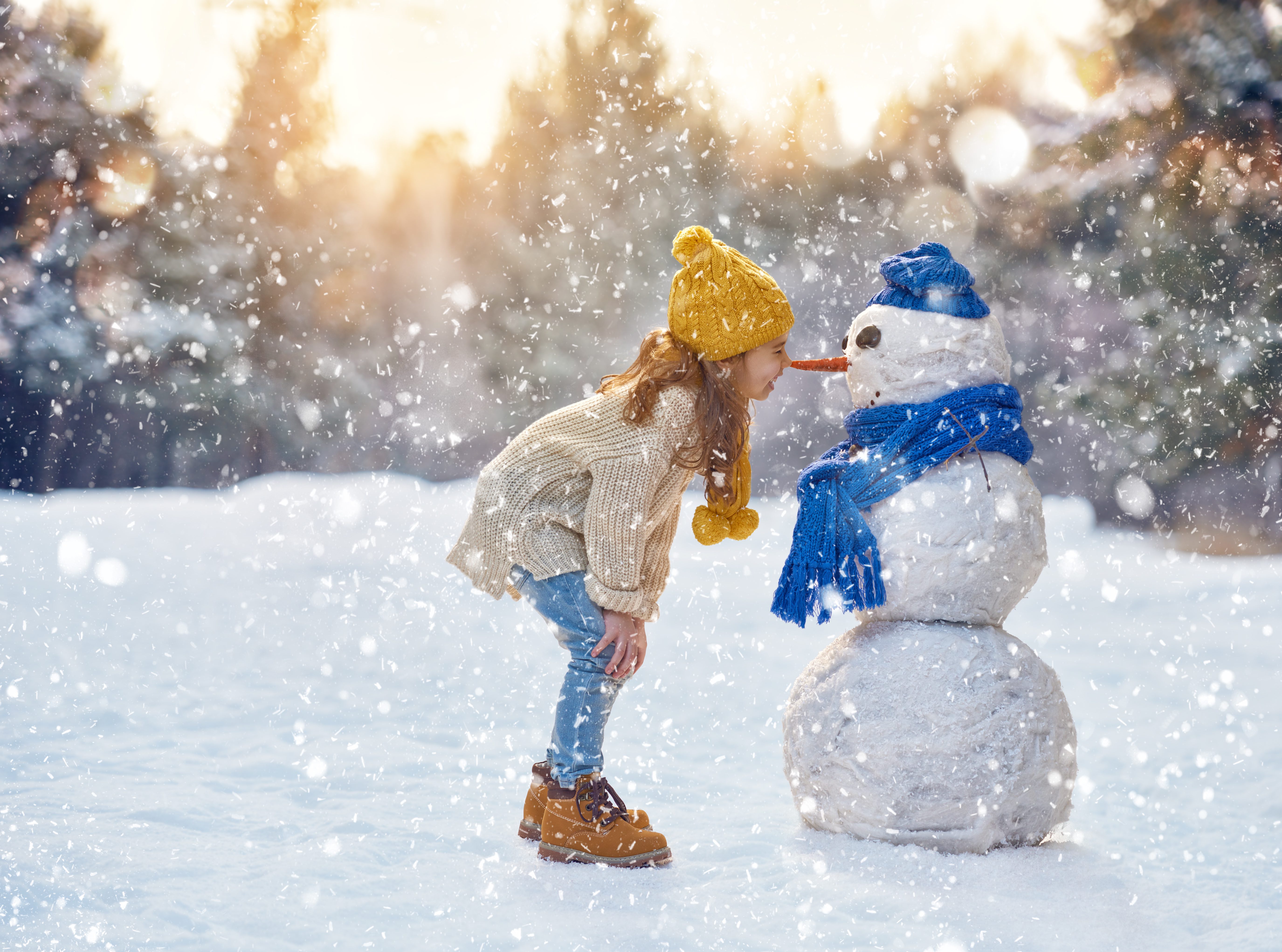 Little girl smiling with the snowman she built 