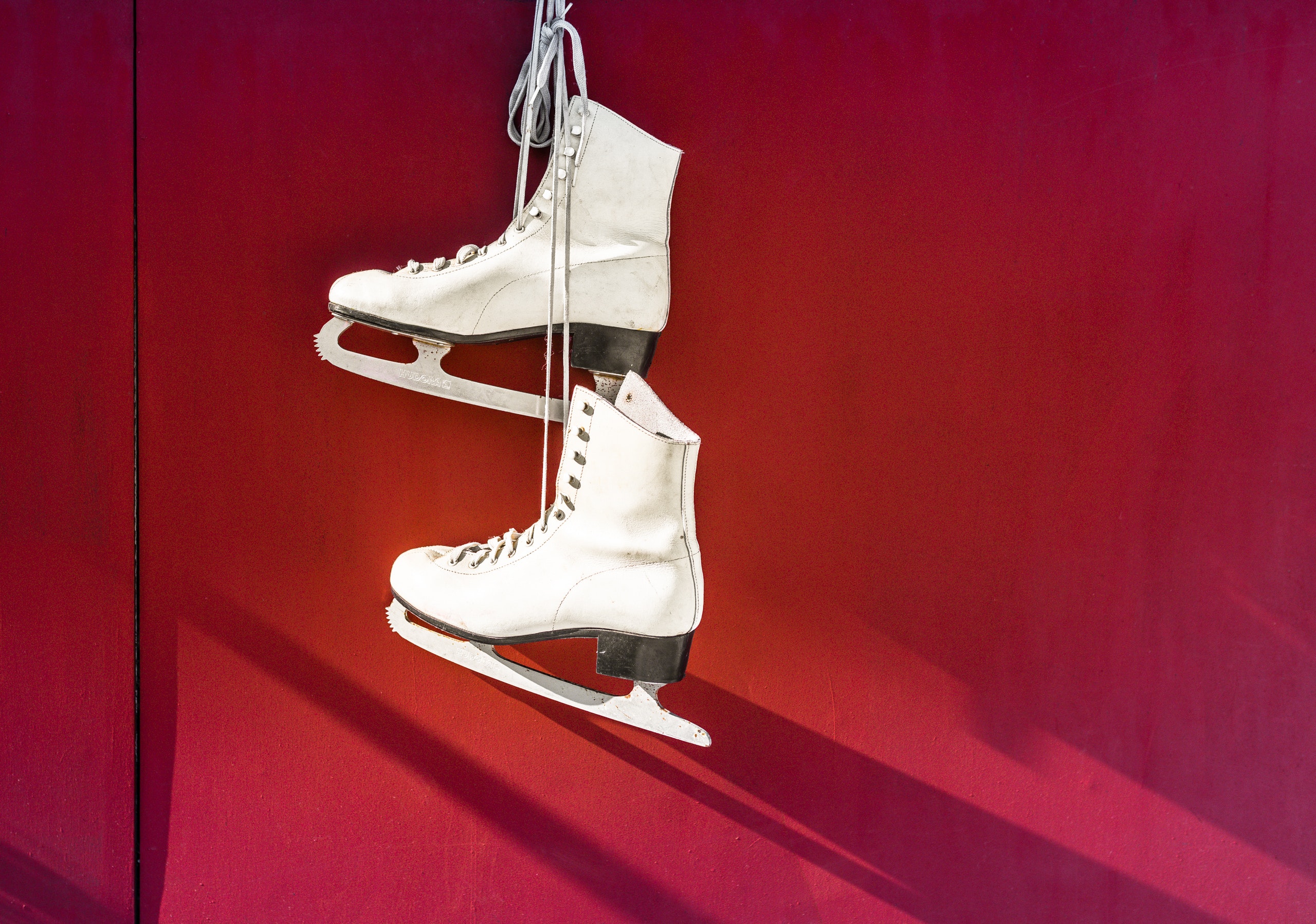 White ice skates hanging on a red wall