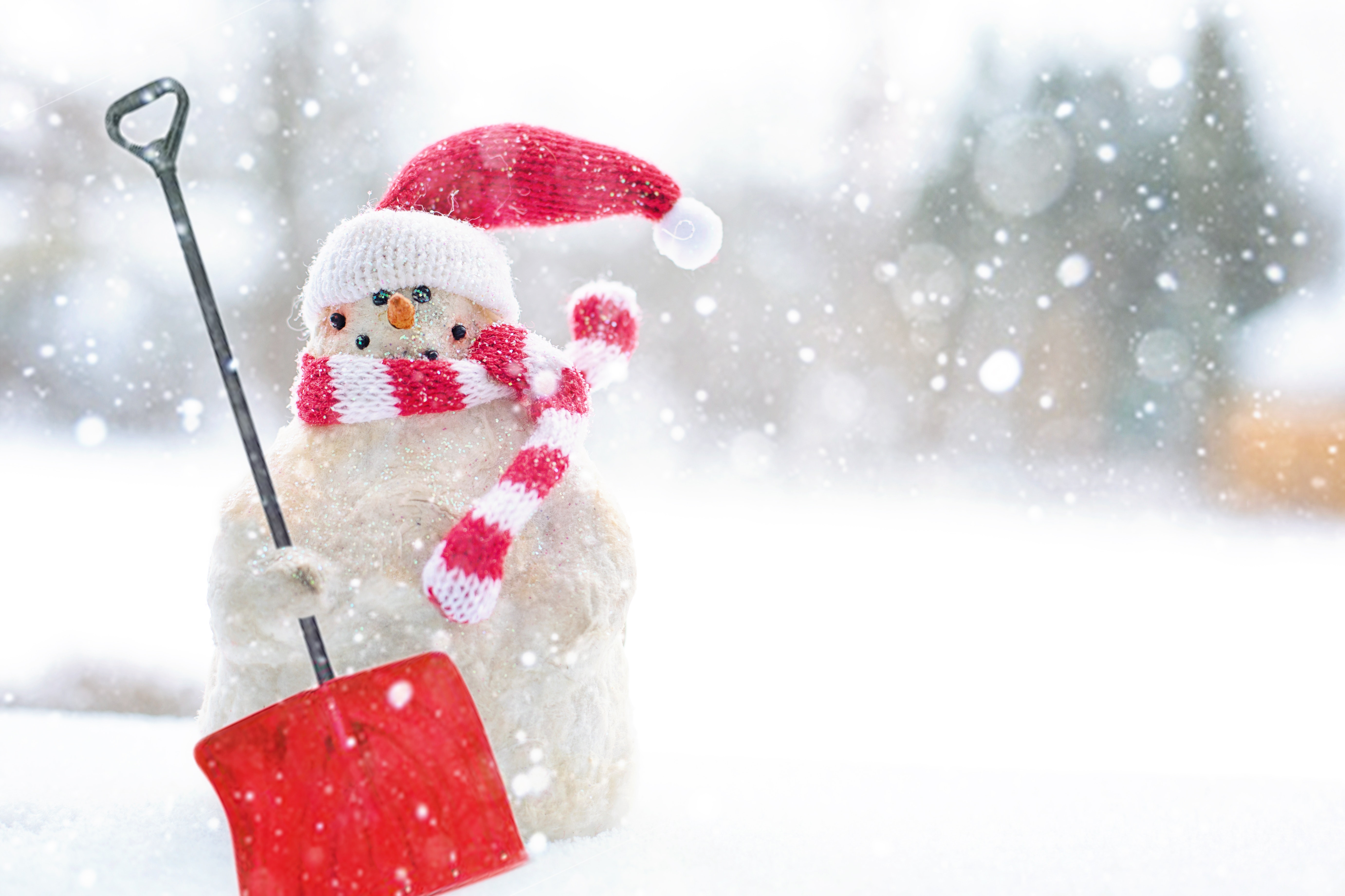 Snowman holding wearing a santa hat holding a red snow shovel