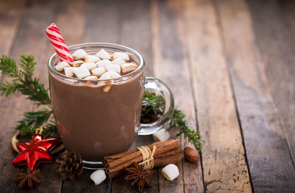 Hot coco with marshmallows, and a candy cane on a wood table with cinnamon sticks