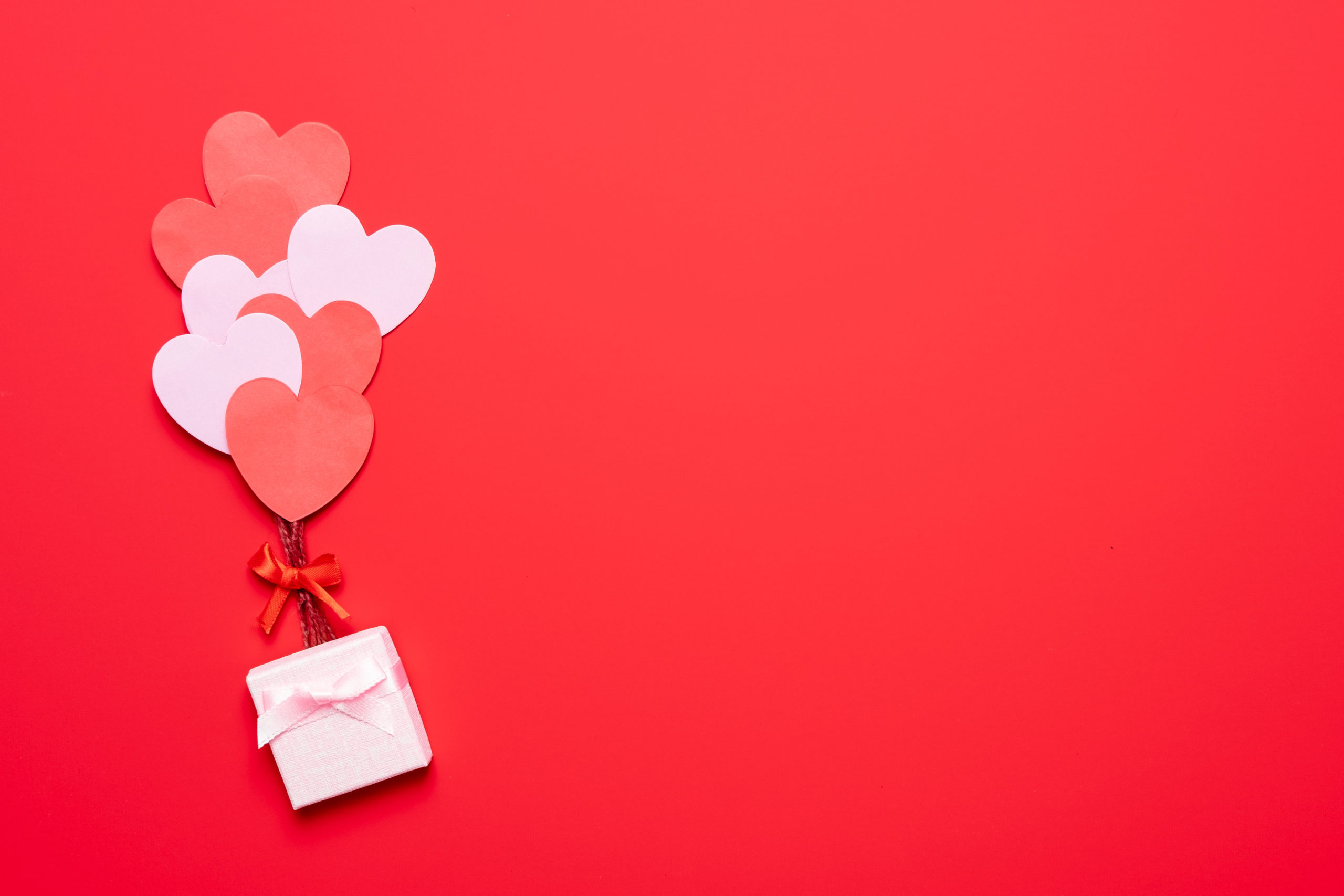 Red background with balloon hearts lifting a pink present