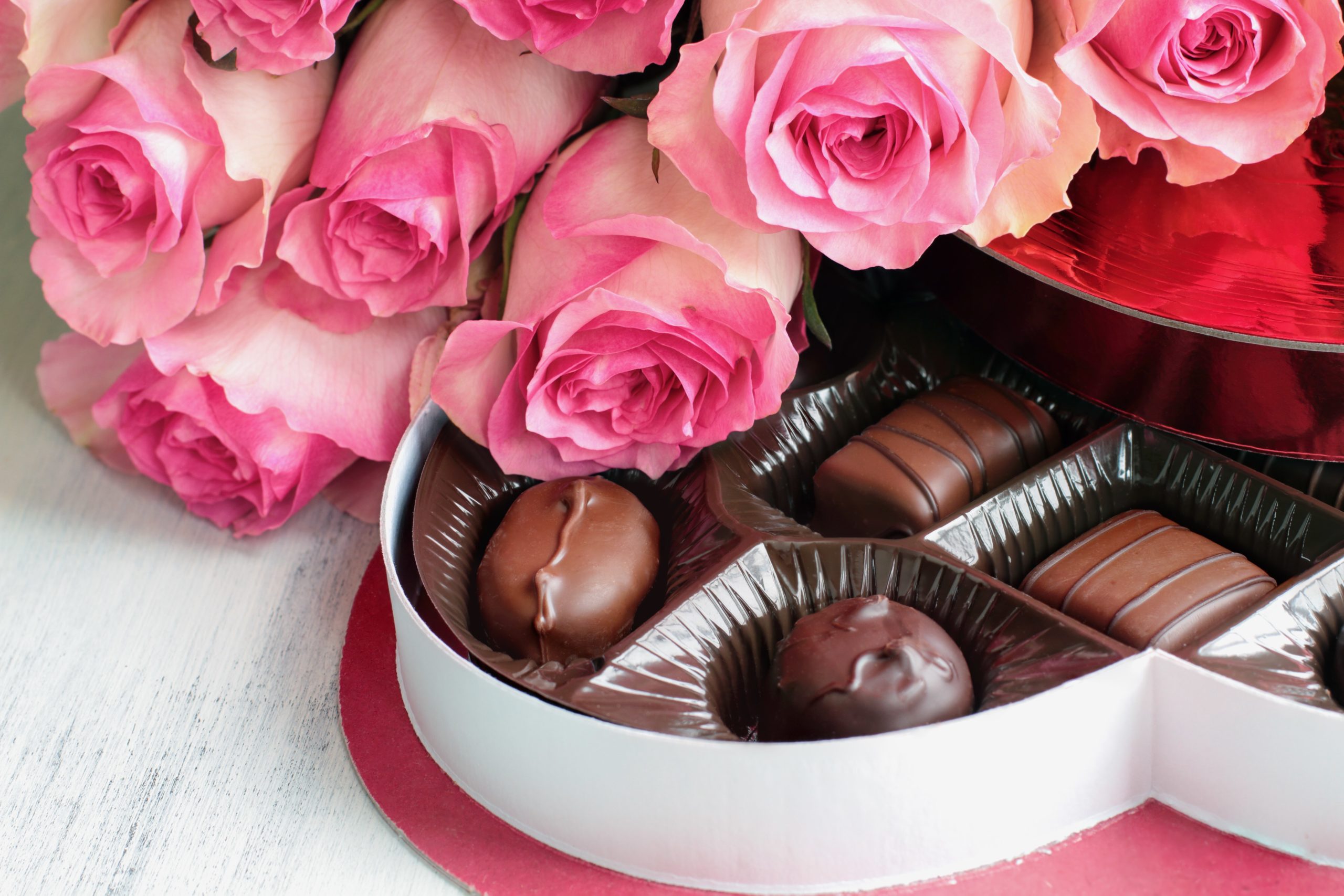 Pink roses and chocolates in a heart box on a white table