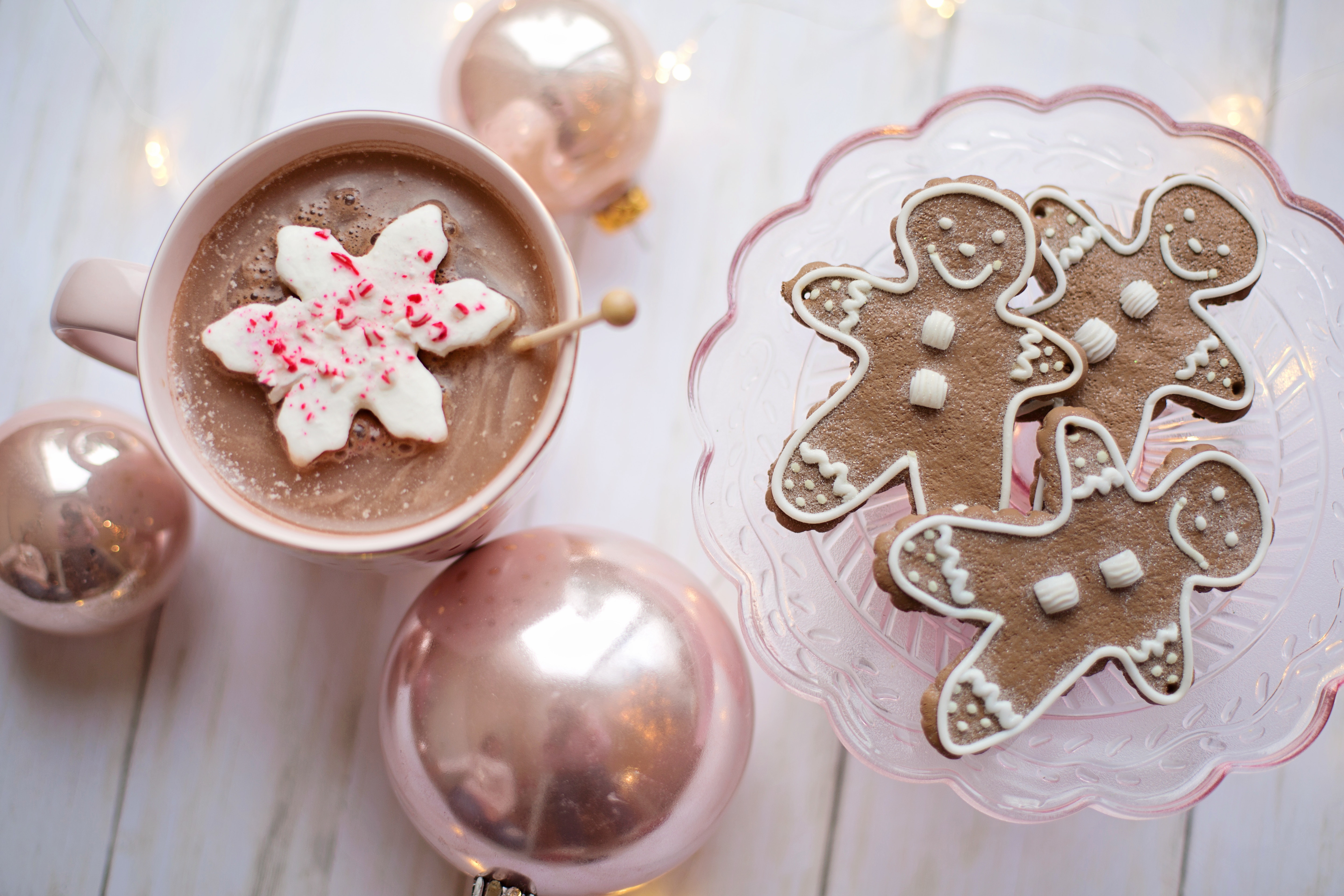 Hot chocolate and gingerbread cookies on a light wood table with pink decor accents