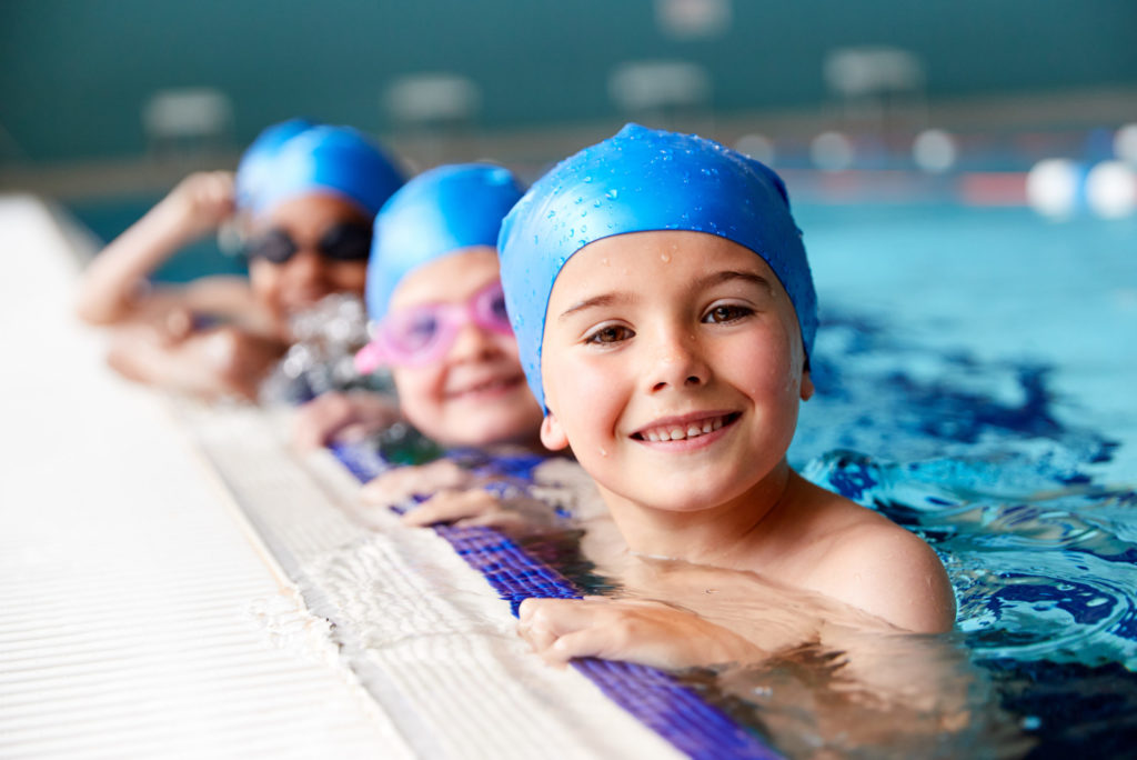 Kids in blue swim caps in a swimming pool holding the edge of the pool