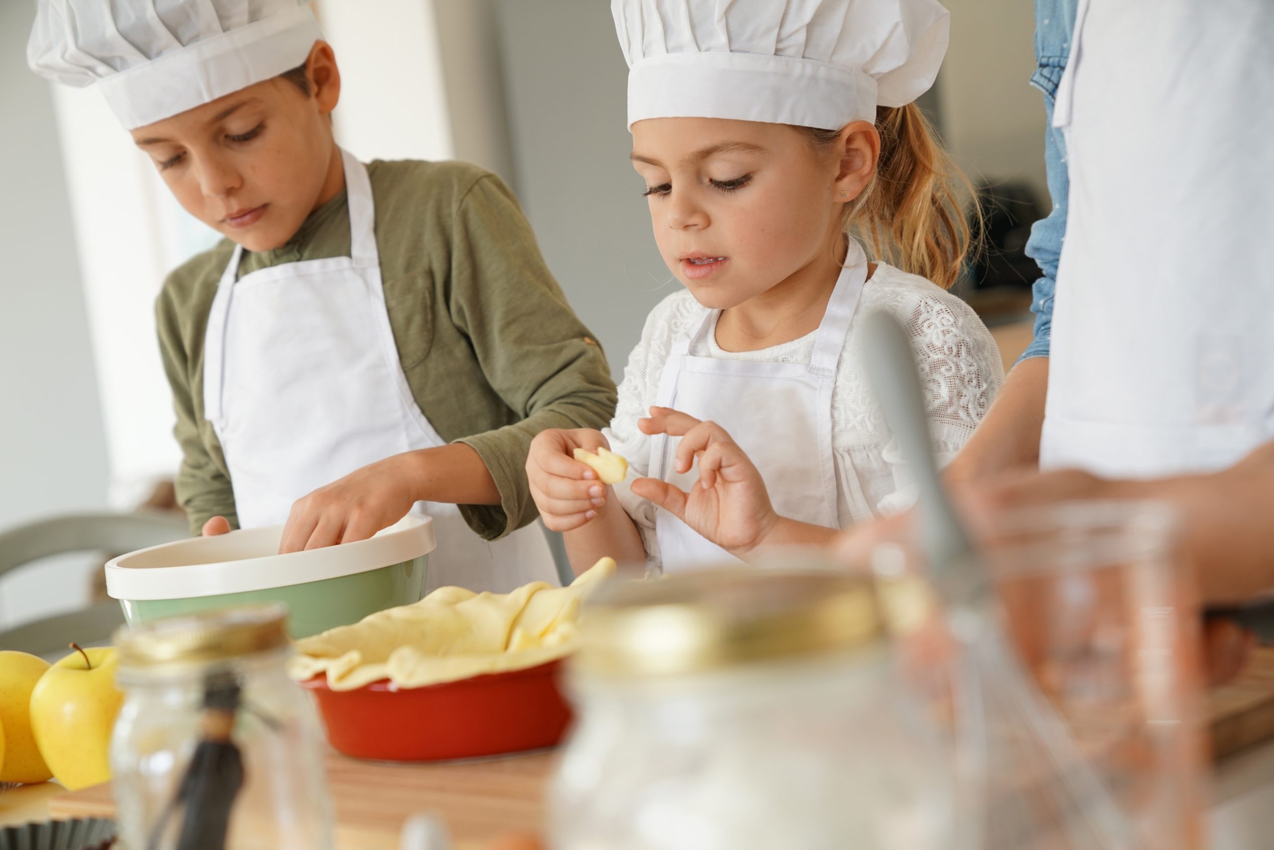 Two children in chef hats making apple pie crusts