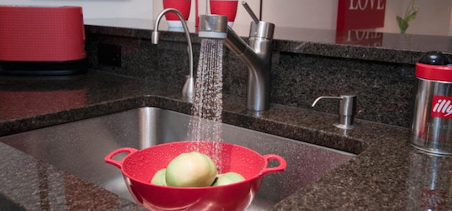 A stainless steel sink with running water washing fruit.
