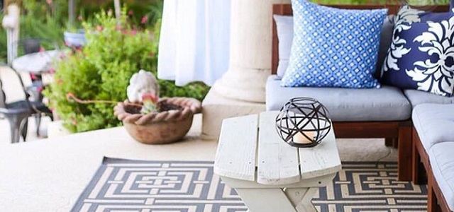 An outdoor patio living space with blue throw pillows and a patterned grey rug.