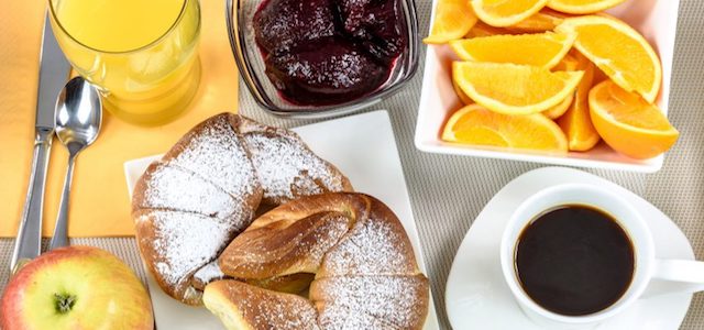 A brightly colored tray of breakfast foods, like sliced oranges, an apple, and orange juice.