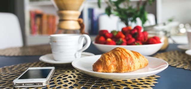 A morning breakfast with a golden croissant, coffee, and red strawberries.