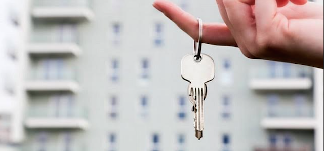 A hand holding silver keys to a apartment.