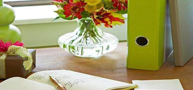 An organized wooden desk with a green binder, white paper, and fresh flowers in a vase.