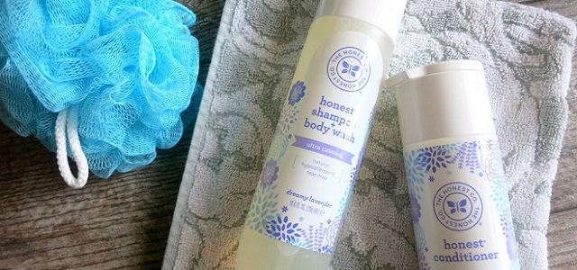 A bath set of shampoo and conditioner from The Honest Company with a wash cloth and loofa on a wooden table.