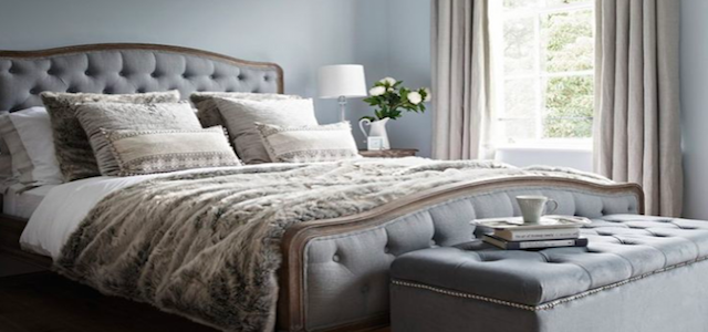 A luxury white and grey bedding set with a storage trunk at the end fo the bed.