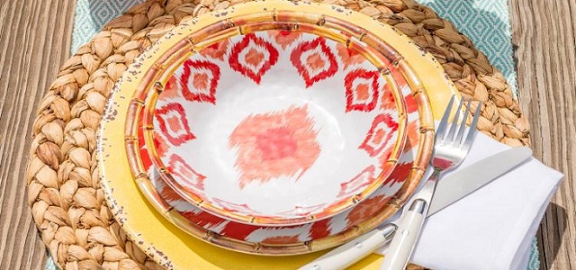 A brightly colored coral, orange, and yellow dish set on a wicker place mat.
