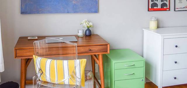 A wooden desk and clear plastic chair set up next to a filing cabinet.