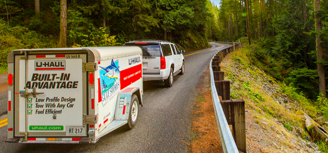 A white SUV pulling a UHAUL trailer on a back country road.
