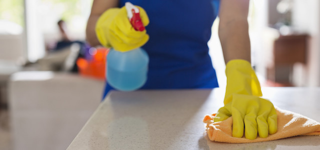 Woman cleaning kitchen counter wearing yellow gloves.