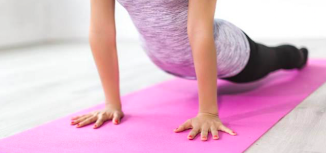 A woman stretching on a hot pink yoga mat in a home gym.