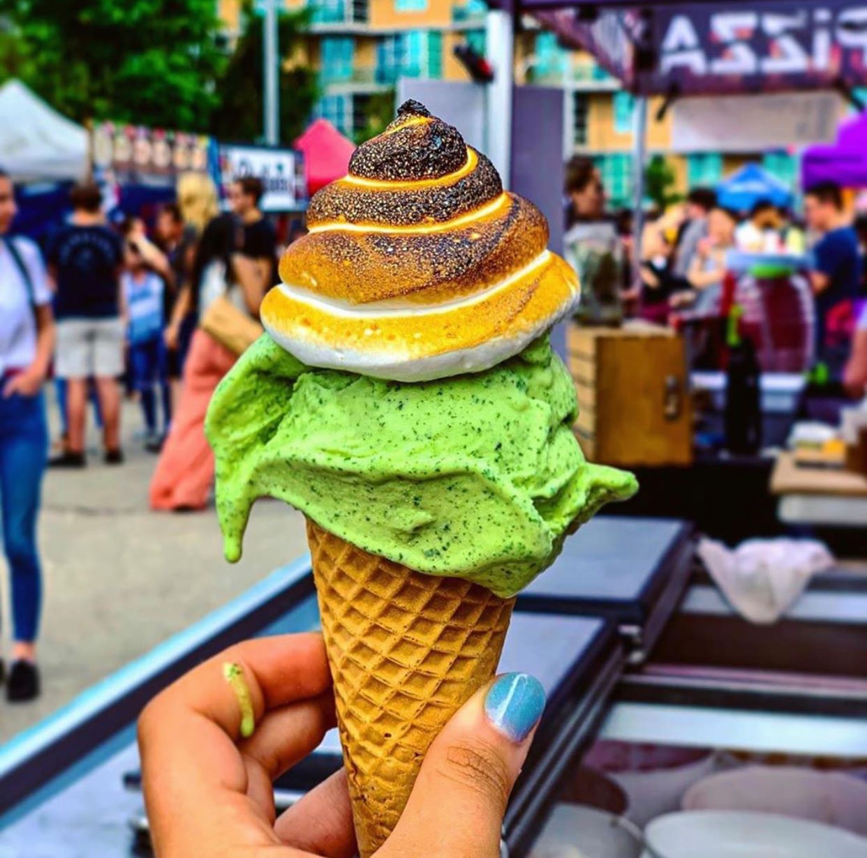 Person holding ice-cream cone with marshmallow on top of green ice-cream 