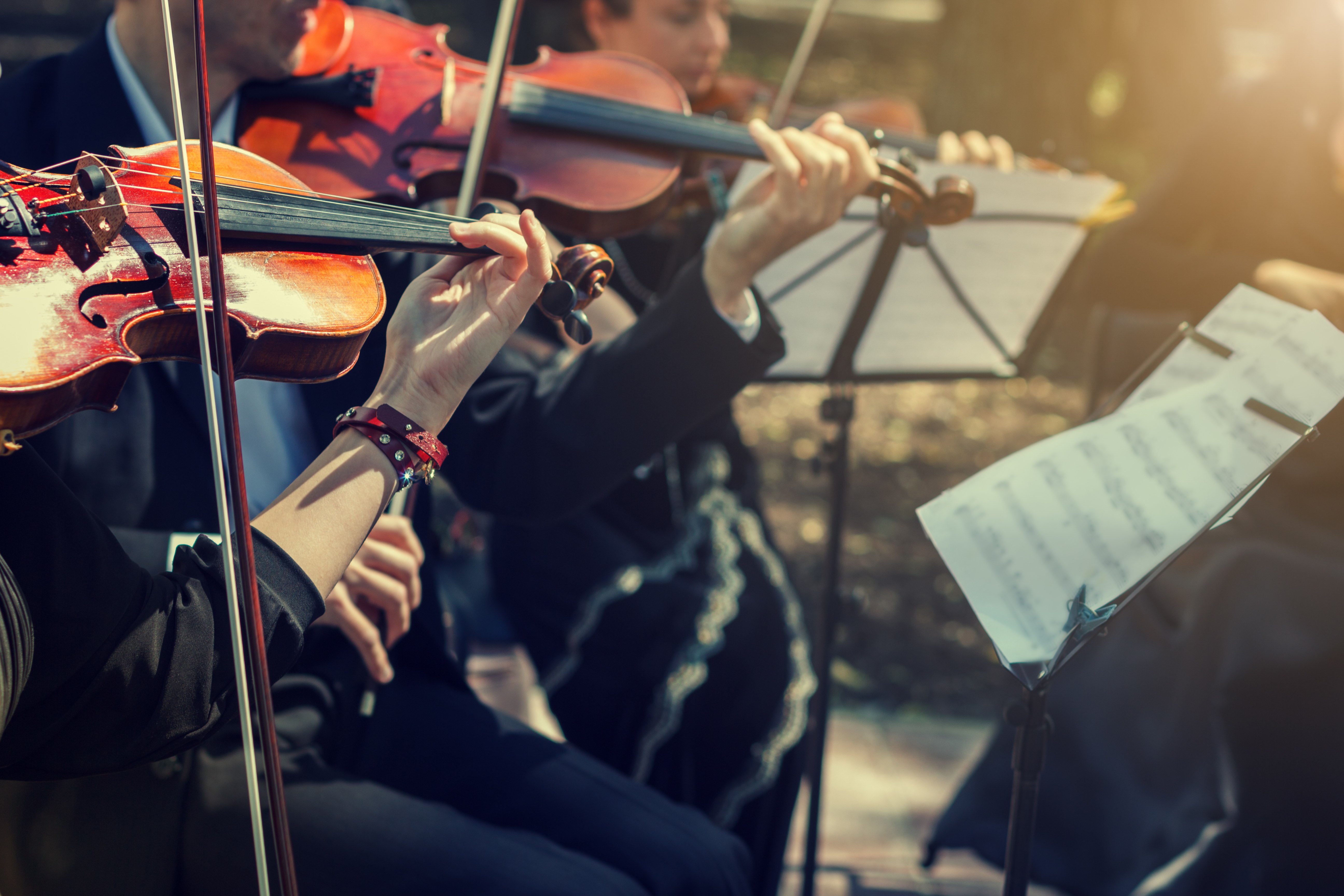 Boys playing the violin on a stage in an outdoor concert.