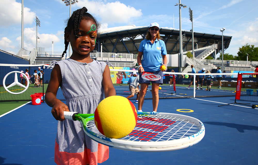 Young child balancing tennis ball on racket 