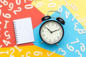 An alarm clock and notebook laying on top of colorful paper with numbers in white