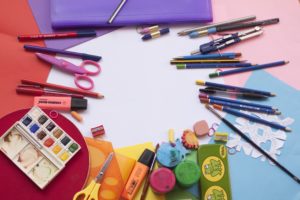 Colorful school supplies displayed on a white table, markers, paint, colored paper, scissors, erassers