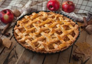 A freshly baked apple pie on a table with apples in background