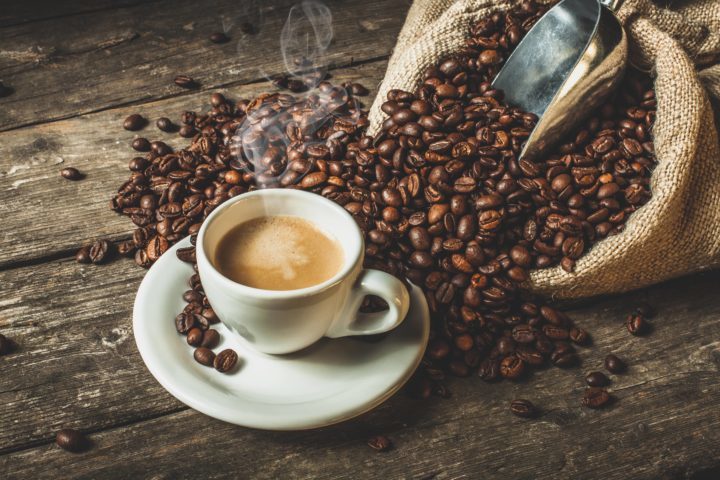 A cup of steaming hot coffee with coffee beans 