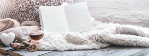 Cozy throw blanket, tea and book open on a couch