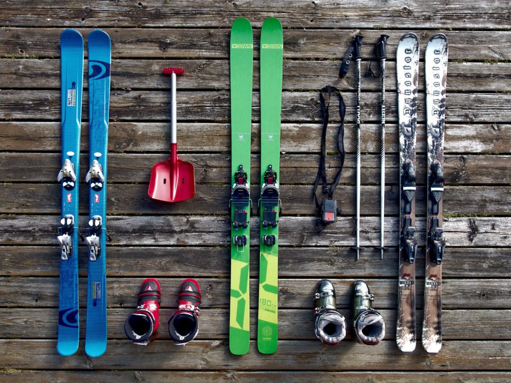 Ski and snow equipment, a shovel, skis, boots, and poles lined up on a wood floor