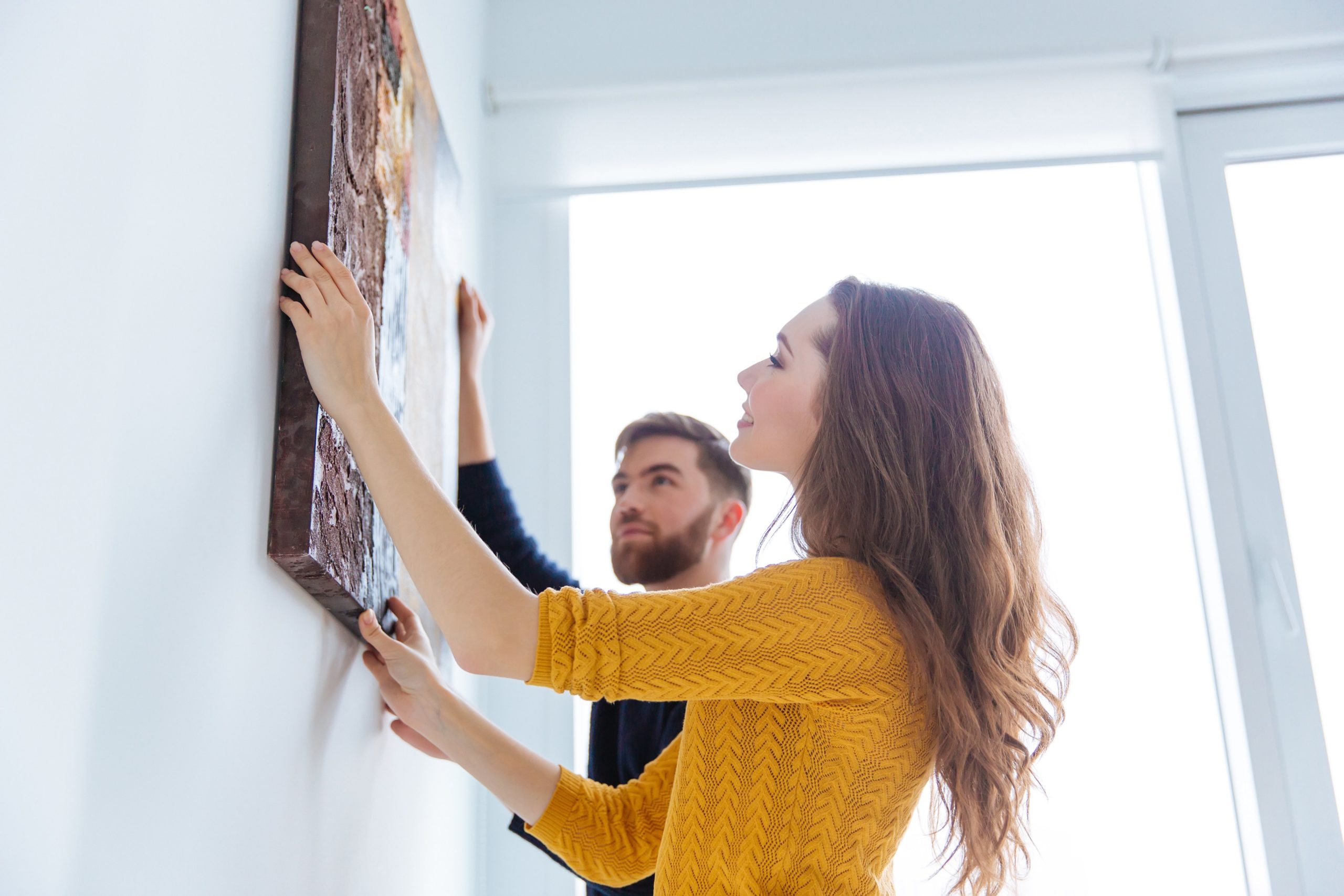 A couple hanging a canvas painting in their home on a blank wall