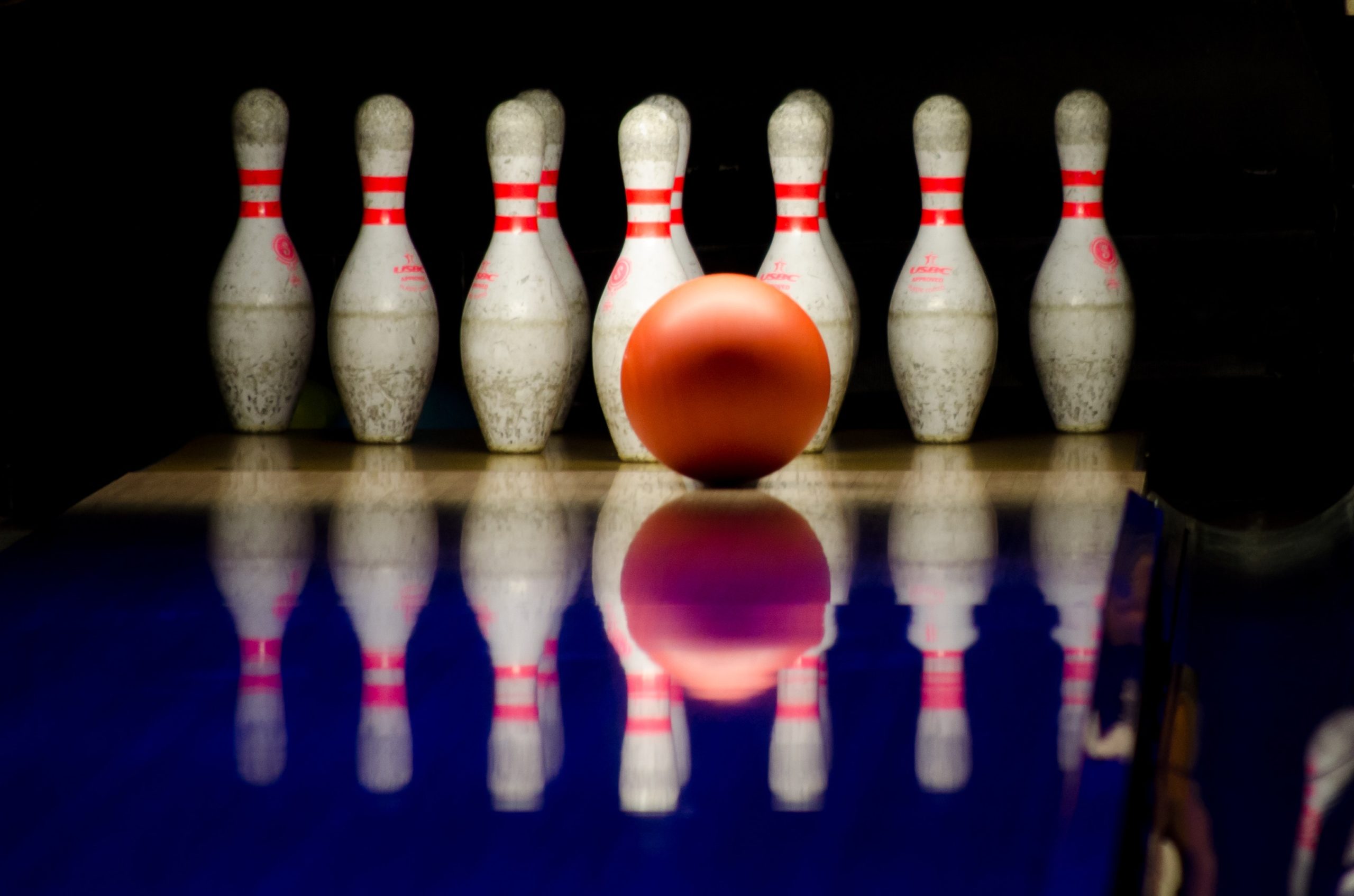 A closeup shot of a bowling alley lane with a ball rolling towards the pins