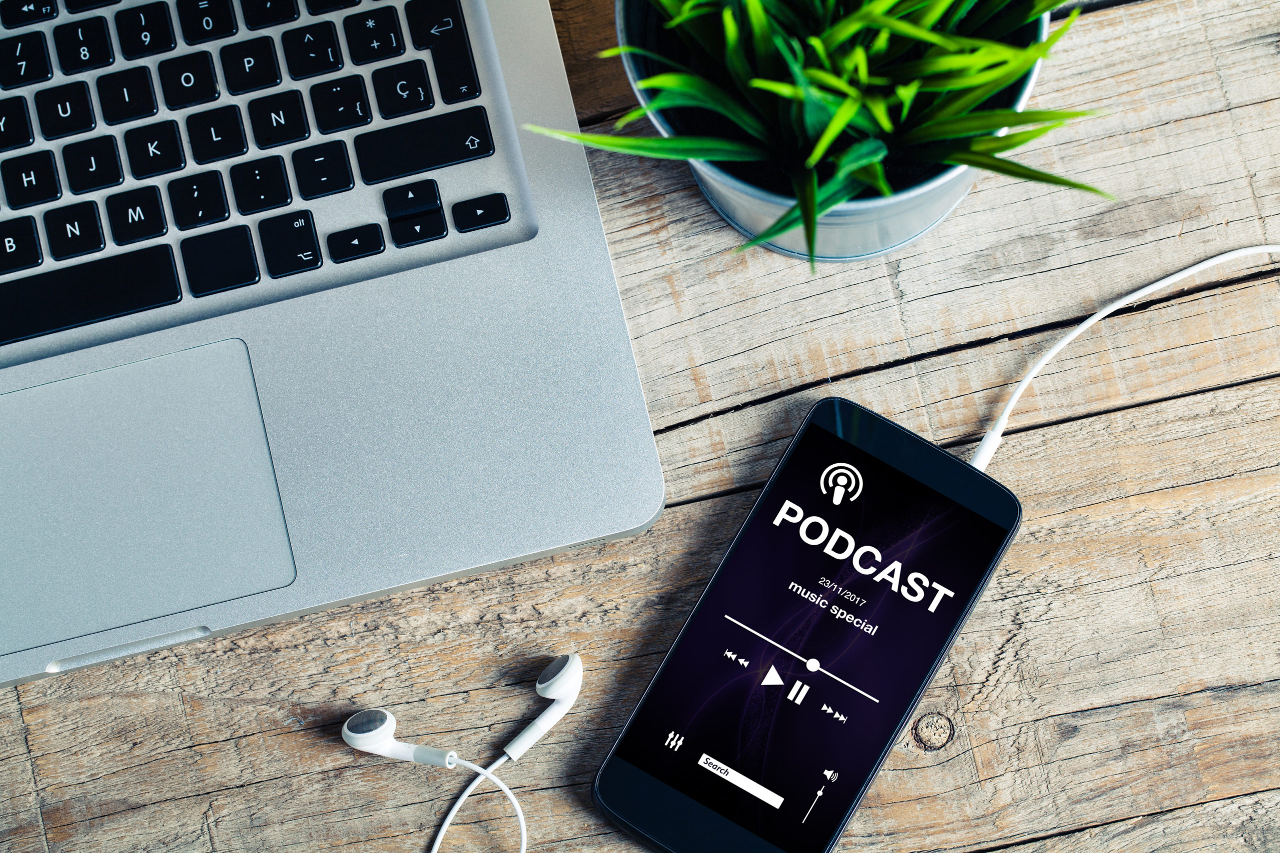 A phone with a podcast playing on a wooden desk with a computer