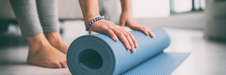 A woman rolling up a yoga mat on the floor