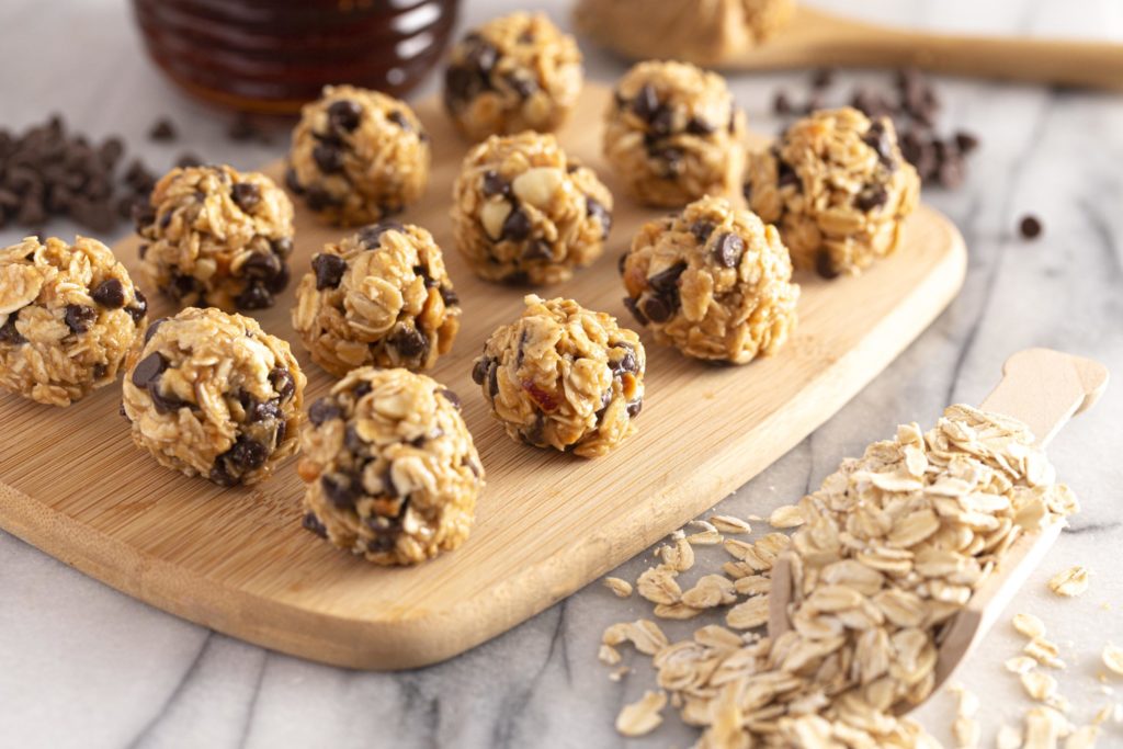 Rolled oat cookies on a cookie board with the ingredients oats, honey and chocolate chips displayed on the countertop