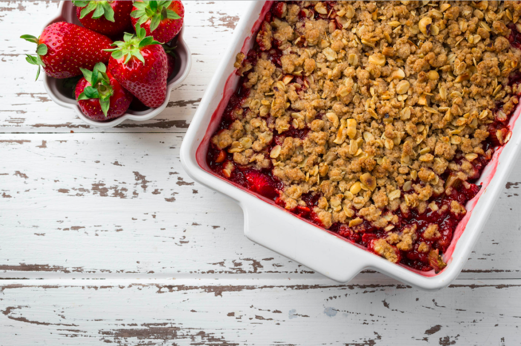 A strawberry crisp in a white cooking plate on a wood table