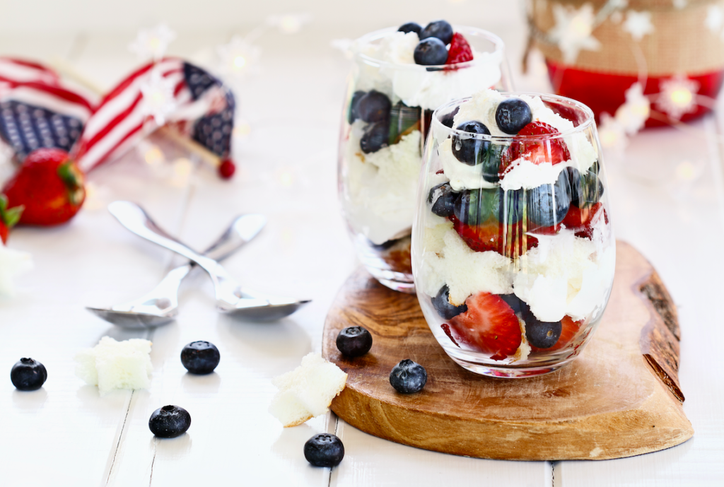 A cup of whipped cream and berries with an american flag on a table
