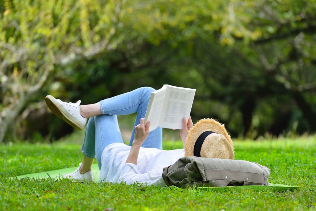 A woman laying on a yoga mat on a grass field reading